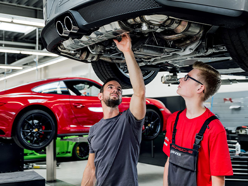 Ein Werkstatt-Mitarbeiter schraubt an der Karosserie eines Porsche Sportwagens.