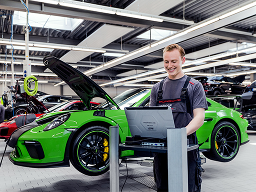 Ein Kraftfahrzeug-Mechatroniker prüft an seinem Laptop einen Porsche Sportwagen.